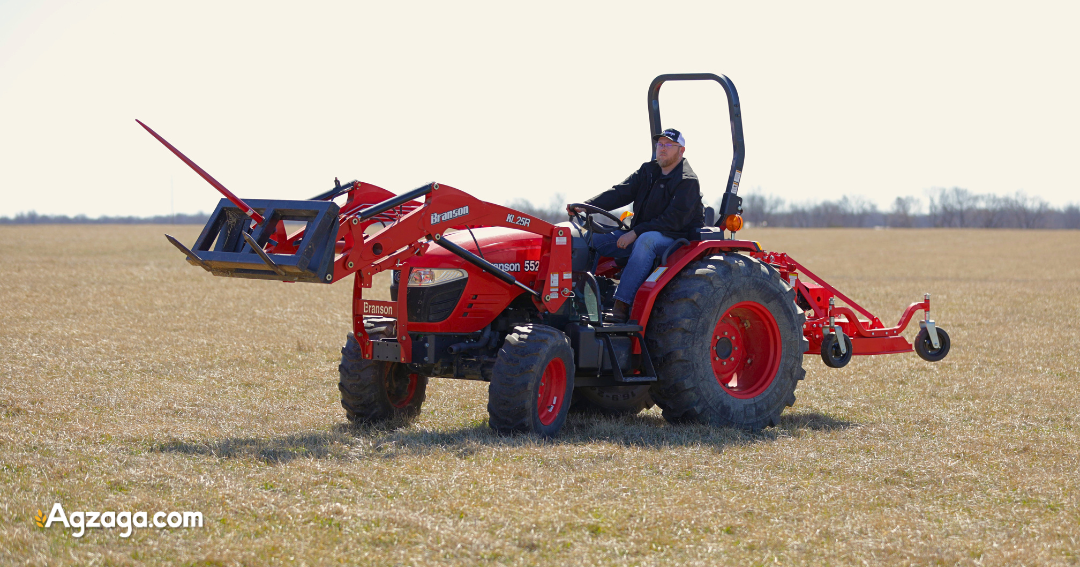 Tractor lifting round hay bale with front-mounted bale spear