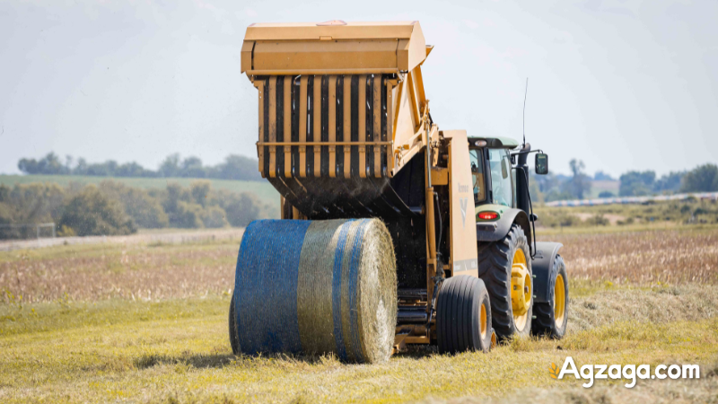 Round baler ejecting a tightly wrapped hay bale in field